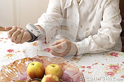 The old woman measures arterial pressure while sitting in the living room at the table. Stock Photo