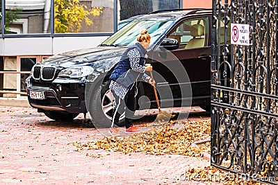Old woman raking fallen leaves in the courtyard, senior woman gardening during autumn season, cleaning the yard in Bucharest, Editorial Stock Photo