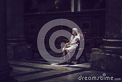 Old woman sitting in colored light on church bench Editorial Stock Photo