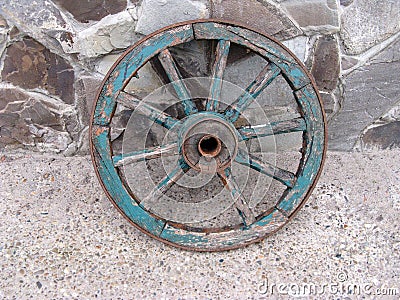 An old wooden cartwheel with a broken spoke. Cracked wooden elements painted with blue paint. Leaning against a stone wall Stock Photo