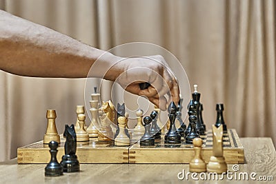 Old wooden chess pieces on chessboard. Hand of adult man making move with white pawn Stock Photo
