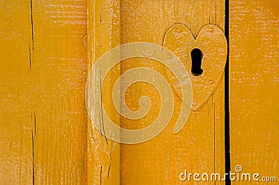 old wooden door in yellow. painted wood texture. metal overlay on the keyhole in the form of heart. background for your company Stock Photo