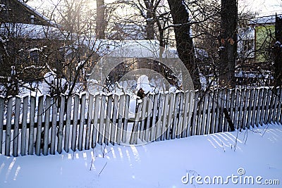 Old wooden fence, snowy suburban area and sun glare Stock Photo
