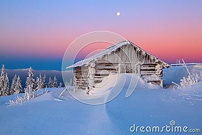Old wooden hut. Huge snowdrifts around. Background of the high mountains. High fairtrees freezed with snowflakes. Stock Photo