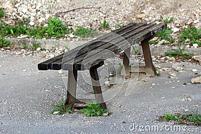 Old wooden public bench with strong rusted metal supports mounted on paved edge of abandoned parking place surrounded with rocks Stock Photo