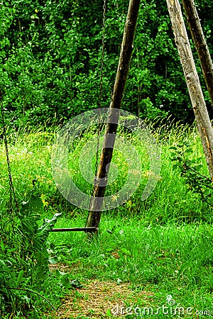 Old wooden rustic garden iron chain hanging swing on green grass background Stock Photo