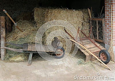Old wooden wheelbarrows, still used, with hay bales, pitchforks and wicker broom. Stock Photo