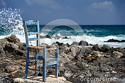 An old, worn-out chair on the rocky coast of the Mediterranean Sea on the island of Crete Stock Photo