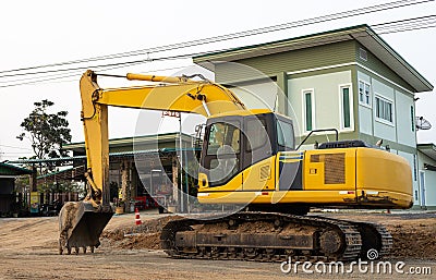 An old yellow backhoe parked on the roadway being renovated near high-voltage power lines Editorial Stock Photo