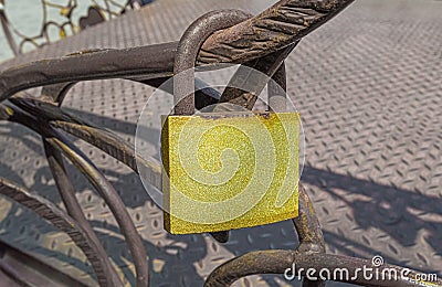 Old yellow glittering padlock with rust hanging on metal fence Stock Photo