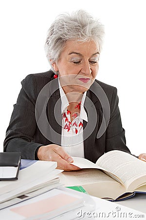 Older business woman sitting at desk reading in a book. Concept Stock Photo