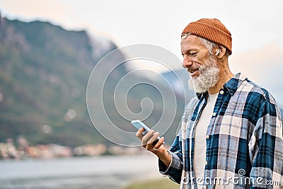 Older elder hipster man standing in nature park wearing earbud using phone. Stock Photo