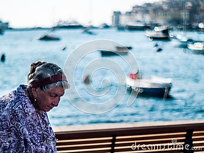 Creative Scene of an old woman from Rovinj, Croatia central Europe in midday, with beautiful boats bokeh balls useful for sample. Editorial Stock Photo