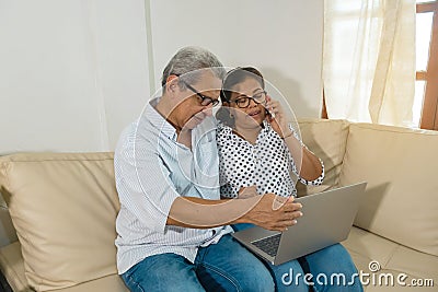 Older Latino web-surfing couple with laptop and cell phone. Stock Photo