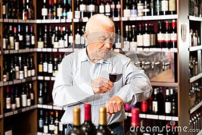 Older man inspecting quality of red wine in wine store in search of perfect wine for solemn occasion Stock Photo