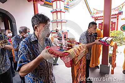 An Older man presenting the offerings in front of the monks while praying in the temple Editorial Stock Photo