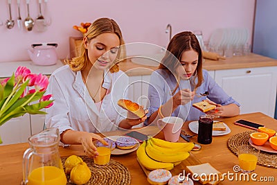 Older sister eating yummy croissant enjoying breakfast with sibling Stock Photo