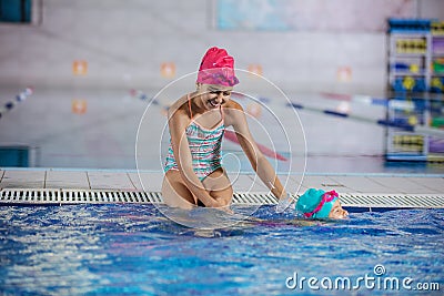 Older sister watching younger one swimming along pool nosing Stock Photo