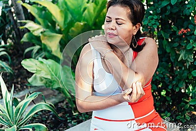 Older woman clutching her elbow in pain while sitting in the park, health concept Stock Photo