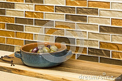 Olives in serving dish and wooden cutting board on engineered stone counter top with glass mosaic tile back splash in home kitchen Stock Photo