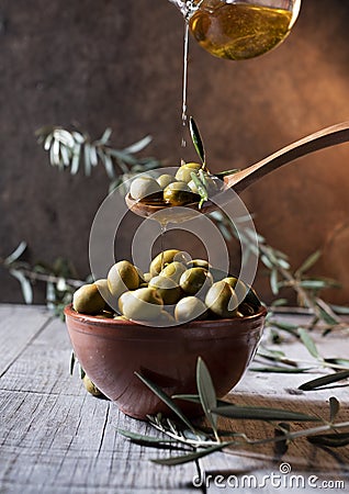 Olives in wooden spoon pouring oil over bowl full of olives with bone Stock Photo