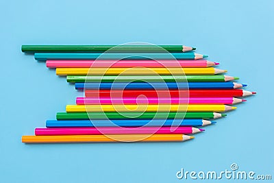 Ð¡olored pencils folded in the shape of an arrow indicating the direction on blue background. Stock Photo