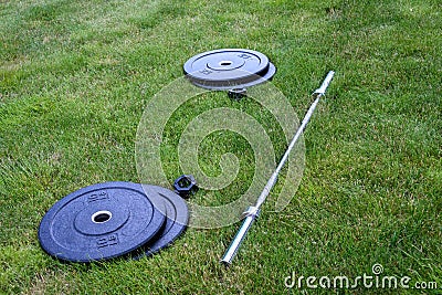 Olympic barbell with black weight plates on a green lawn, ready for an outdoor workout Stock Photo