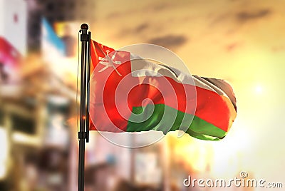 Oman Flag Against City Blurred Background At Sunrise Backlight Stock Photo