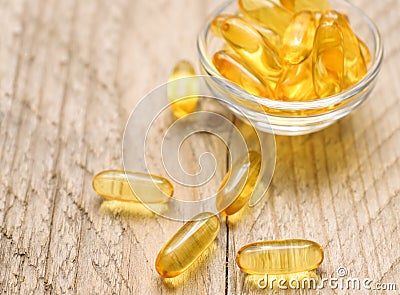 Omega 3 fish liver oil capsules in small glass bowl. Close up of golden translucent pills. Healthy fatty acids nutritional Stock Photo