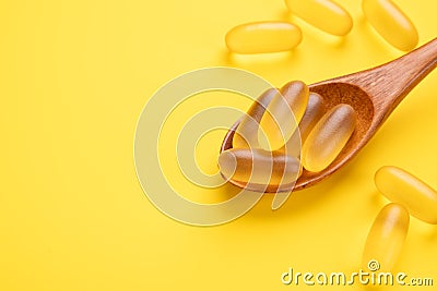Omega 3 pills in wooden spoon on yellow background. Fish oil softgels. Close up. Top view. Copy space Stock Photo
