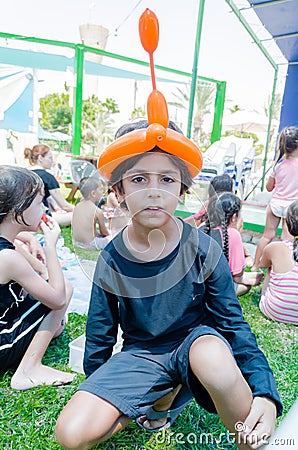 Omer, ISRAEL -Teenager sitting on the grass with other children with inflatable ball on his head in the form of a turban Editorial Stock Photo