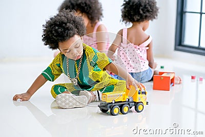 One African mixed race boy is playing with truck toys in front of the other girls and look enjoy and happy with this activity Stock Photo