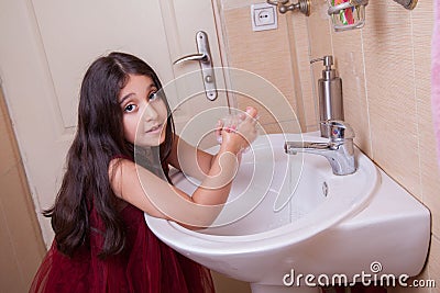 One beautiful little middle eastern arab girl with red dress is washing her hands in the bathroom. Stock Photo