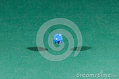 One blue dice falling on a green table Stock Photo