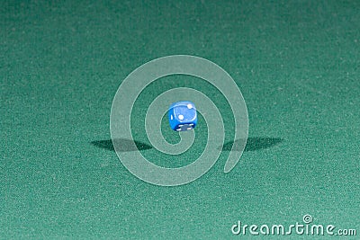 One blue dice falling on a green table Stock Photo