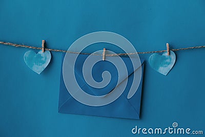 One blue envelope hanging on rope isolated blue background with two blue hearts on the sides. Write a letter to a friend. Stock Photo