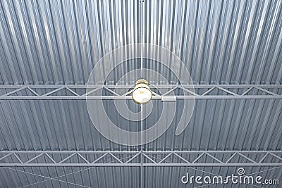 One bulb hanging from the ceiling under a metal lattice in a large industrial warehouse. Stock Photo