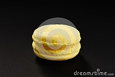 One cake of macaroni yellow lemon color. Delicious macaroon isolated on black background. French sweet cookie Stock Photo