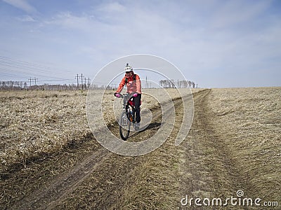 One cyclist in bright clothes rides on the field road among the endless steppes in spring Stock Photo