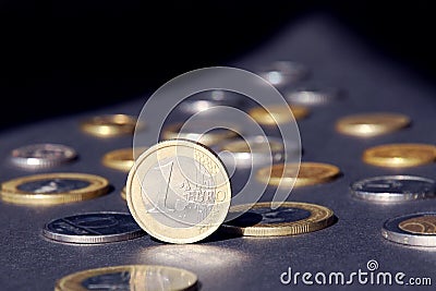 One euro coin stand on edge shining in sunlight, many different coins on dark background. Money flow Stock Photo