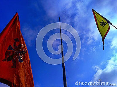 One flagpole with no flag, and two flags of orange and yellow color with the picture of goddess Hanuman. Stock Photo