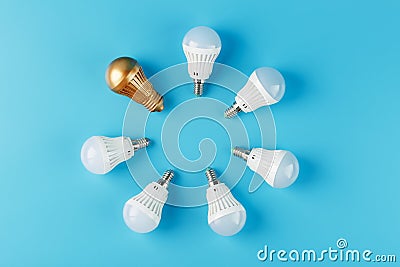 One Golden light bulb in the circle of a ring of energy-saving white lamps on a blue background Stock Photo