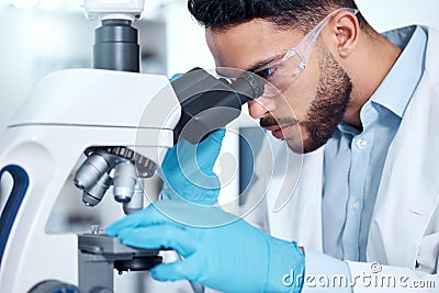 One handsome young mixed race man with a dark beard wearing gloves and a labcoat and looking at medical samples on a Stock Photo