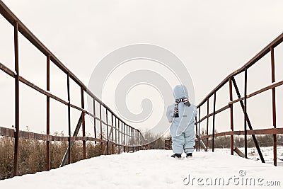 One little boy is standing on a snow-covered bridge across the river. The concept of loneliness and abandonment Stock Photo