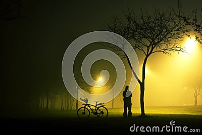 One man is standing and holding the bicycle in foggy and mysterious park. Stock Photo