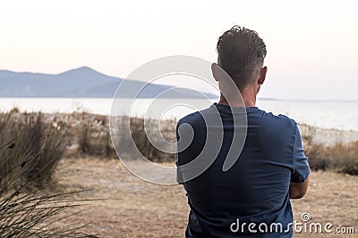 One man viewed from back in landscape contemplation. Tourist looking scenic place destination with ocean and island. Travel people Stock Photo
