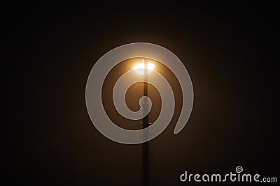 One night lamppost shines with faint mysterious yellow light through evening fog Stock Photo