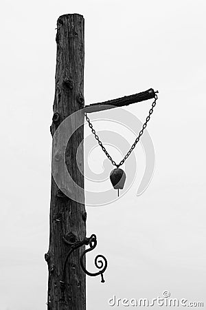 One old bell used at the farm mounted on a wood tree pillar - Black and White Stock Photo