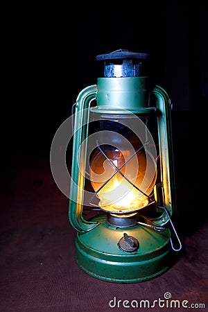 Old worn kerosene lamp green is in the dark of night on Burgundy background Stock Photo