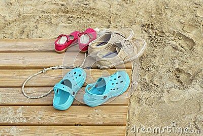 Adult and childrens` shoes on wooden boardwalk with sand at beach Editorial Stock Photo